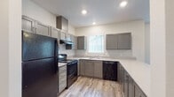 Located at 1295 NE Territorial Rd in Canby, Oregon, this single-story unit offers a well-organized layout that balances functionality with modern design. The kitchen serves as a central highlight, featuring gray shaker-style cabinetry paired with light countertops and wood-look vinyl plank flooring. Black appliances — including a refrigerator, gas range with overhead ventilation, and dishwasher — provide a bold contrast against the neutral palette. A window above the sink allows natural light to brighten the workspace, and a peninsula counter creates a natural transition into the open living area, where the same wood-look flooring continues before giving way to plush carpeting.

The living space is open and airy, with neutral walls and recessed lighting contributing to a clean, welcoming atmosphere. The bedrooms are carpeted and well-lit, each featuring windows dressed with vertical blinds that offer views of the surrounding area. The bathroom is neatly appointed with a gray vanity, light countertop, drop-in sink, a large mirror, and an overhead light fixture, with a tub and shower area alongside. Throughout the unit, a consistent use of gray tones, neutral walls, and modern finishes creates a cohesive and move-in-ready environment.