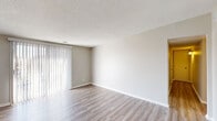 This single-floor residence offers a clean, neutral aesthetic throughout its well-organized layout. The main living area is anchored by light wood-look luxury vinyl flooring that runs seamlessly from the front entry to the sliding glass door, which is dressed with vertical blinds and allows an abundance of natural light to fill the space. The textured ceiling adds subtle dimension to the open living area, which flows comfortably from the entry door toward the glass door access point.

The bedrooms feature plush wall-to-wall carpeting in a warm neutral tone, providing a soft and comfortable underfoot feel. Each bedroom is enhanced by windows fitted with horizontal blinds, offering both natural light and privacy. One bedroom features a notably large window with an outdoor view of greenery, bringing a refreshing natural element into the space.

The overall color palette is cohesive and understated, with soft greige walls and white trim throughout, creating a bright and move-in-ready atmosphere. The floorplan, as seen in the dollhouse view, reveals a thoughtfully arranged interior with defined living, sleeping, and utility zones. The combination of hard flooring in the common areas and carpet in the private rooms reflects a practical and comfortable design suited for everyday living.