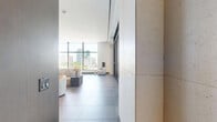 Located at 1142 SW Second Ave in Miami's vibrant Brickell neighborhood, this single-floor space exemplifies contemporary urban design. The open-plan layout is anchored by expansive floor-to-ceiling glass windows that flood the interior with abundant natural light while framing sweeping views of the Miami city skyline and surrounding greenery.

The living area is thoughtfully designed with large-format tile flooring throughout, contributing to a seamless, cohesive aesthetic. A striking built-in dark wood media wall with integrated shelving and display niches serves as a focal point, complemented by curated modern furnishings and sculptural accent pieces. Sliding glass doors open directly to an outdoor terrace adorned with tropical palms, blurring the boundary between interior and exterior.

The dining and kitchen zone features a substantial marble-topped dining table beneath a statement circular pendant light, paired with a sleek kitchen outfitted with dark cabinetry, a decorative mosaic tile backsplash, and high-end stainless steel appliances. A dedicated lounge area with minimalist rounded seating and a small accent table offers a refined setting for relaxation, bathed in natural light from the oversized glazed facade. Vibrant contemporary artwork accents the space, adding bold color and personality to the modern, polished atmosphere throughout.