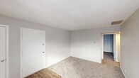 This single-floor unit is designed with a clean, neutral aesthetic throughout. The living areas feature light-toned carpet paired with hardwood-style flooring at key transition points, creating a functional and cohesive look. Walls are finished in soft gray tones, complemented by white trim and textured ceilings that add subtle visual depth. Multiple rooms benefit from natural light admitted through horizontal-blind-fitted windows, offering views of the surrounding exterior.

The kitchen is a practical highlight, equipped with white shaker-style cabinetry accented by matte black hardware, a classic subway tile backsplash, light-toned countertops, a double stainless steel sink with a matte black faucet, and stainless steel appliances including a range and microwave. The bathroom features a full soaking tub surrounded by crisp white subway tile and fitted with matte black fixtures, contributing a timeless, clean finish.

Bedroom spaces are carpeted and well-proportioned, each with ample natural light. The layout, visible in the floor plan image, reveals a thoughtfully organized arrangement of living, sleeping, and kitchen areas, all contained within a compact, efficient single-level footprint.