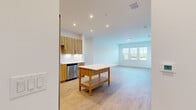 This thoughtfully designed single-floor residence offers a clean, contemporary aesthetic carried consistently throughout every room. The open-concept kitchen is a standout feature, outfitted with warm wood-grain cabinetry, white quartz countertops, a full suite of stainless steel appliances including a refrigerator, range, microwave, and dishwasher, and a freestanding kitchen island that provides additional prep and storage space. Light hardwood flooring runs through the main living areas, enhancing the bright, airy feel. The living area flows naturally from the kitchen and benefits from a wide multi-pane window that frames outdoor greenery views and fills the space with natural light. A glass door provides direct access to an outdoor balcony. The bedrooms feature plush carpeting, ceiling fans, and windows overlooking lush surroundings, with closet storage included. The primary bathroom is finished with wood-tone cabinetry, a white quartz vanity, wood-look flooring, and a glass-enclosed walk-in shower with tile surround. A second full bathroom mirrors the same design language and includes a tiled soaking tub. Recessed lighting, white walls, and clean architectural lines create a cohesive, modern ambiance throughout the entire residence.