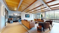 Located at 350 Old Hickory Blvd in Nashville, TN, this generously sized single-floor amenity space offers a sophisticated blend of modern design and comfortable functionality. The centerpiece lounge area makes a striking impression with its warm wood-beamed ceiling, light hardwood flooring, and an abundance of natural light streaming through large windows. Multiple seating arrangements — including leather sofas, upholstered accent chairs, and built-in banquette seating — provide versatile gathering options throughout the space. A dedicated lounge zone features textured wallcoverings, curated artwork, and warm amber leather chairs anchored by a decorative area rug, creating an inviting and refined atmosphere. The full-length kitchen is appointed with sleek grey cabinetry, dark countertops, stainless steel appliances, a hexagonal tile backsplash, and glass-front upper cabinets — all illuminated by linear recessed lighting. A private dining nook with high-back upholstered booth seating and a wood-top table offers an intimate setting for smaller gatherings. Throughout, light hardwood floors, carefully selected furnishings, mounted flat-screen displays, and thoughtfully placed artwork contribute to a cohesive, upscale aesthetic that balances style with practicality.