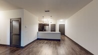 This single-story unit presents a well-designed, modern layout with consistent finishes throughout. The open-concept living and kitchen area serves as the heart of the space, where rich, dark wood-style plank flooring extends seamlessly across the main areas, complemented by bold dark baseboards and crisp white walls. A ceiling fan enhances the spacious living area, which receives natural light through a window overlooking greenery.

The kitchen is thoughtfully appointed with dark espresso cabinetry, white countertops, and a full suite of stainless steel appliances, including a refrigerator with an ice and water dispenser, a range, and an over-the-range microwave. A kitchen island with pendant lighting above provides additional workspace and a natural divide between the kitchen and living areas. Two dark panel-style doors lead to additional spaces from the main area.

Bedrooms feature plush carpet flooring, natural light from windows with blinds, and ceiling fans. A half bathroom offers wood-style flooring, a pedestal sink, and a toilet. The full bathroom includes a glass-enclosed tiled shower, a dark vanity with a white countertop, and wood-style flooring. A dedicated laundry room houses a full-size washer and dryer with overhead wire shelving for storage.