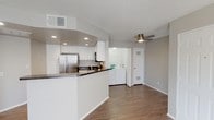 This single-floor residence offers a practical and comfortable layout designed for everyday living. The open-concept design connects the kitchen and living area seamlessly, creating a spacious and functional environment. The kitchen is a standout feature, outfitted with crisp white cabinetry, dark granite countertops, and a full suite of stainless steel appliances including a side-by-side refrigerator, gas range, and over-the-range microwave. Recessed lighting illuminates the kitchen, enhancing its clean, modern aesthetic. A peninsula-style counter provides additional prep space and serves as a natural divider between the kitchen and the main living area. The living area is bright and open, with a ceiling fan overhead and warm wood-style flooring that extends throughout the space. A large window fitted with vertical blinds allows natural light to fill the room. A dedicated in-unit laundry area is conveniently tucked nearby, housing a full-size washer and dryer. The bedroom is a quiet, well-sized retreat with matching wood-style flooring and a window that brings in natural light. The bathroom features a full tub-shower combination with white tile surround and ample cabinetry for storage. Textured ceilings are consistent throughout the home.