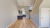 This two-story, 3-bedroom, 2-bathroom home is thoughtfully laid out across two floors, with the main living spaces occupying the more expansive ground level. The open-concept main floor seamlessly connects the living room, dining area, and kitchen beneath soaring vaulted ceilings that amplify the sense of space and invite abundant natural light. The kitchen is a standout feature, showcasing dark espresso shaker-style cabinetry, granite countertops with warm veining, stainless steel appliances, and light hardwood-style flooring that flows throughout the main living areas. A breakfast bar peninsula provides additional counter space and casual seating. Pendant lighting adds a modern, decorative touch overhead. The bedrooms are well-proportioned, each featuring ceiling fans, closets, and the same light hardwood-style flooring, with natural light filtering through window blinds. The primary bedroom offers a generous footprint. The bathrooms include a walk-in shower stall with built-in corner seating. The home also includes five closets for ample storage, two utility rooms, and an attached garage with an automatic opener. A decorative wooden privacy gate completes the exterior, adding charm and security to the property.