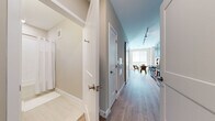 This single-floor residence offers a thoughtfully designed layout that balances comfort and functionality. A central hallway connects the key living areas, finished with smooth hardwood-style flooring that runs throughout the space and contributes to a cohesive, contemporary aesthetic.

The kitchen is fitted with rich dark wood cabinetry, granite countertops, and a full suite of stainless steel appliances including a refrigerator, range, and microwave. Track lighting overhead ensures the workspace is well-illuminated. Adjacent to the kitchen, the dining area provides a welcoming space for meals, bathed in natural light from nearby windows.

The living area is bright and inviting, featuring large windows with roller blinds that allow for flexible light control. A comfortable seating arrangement, anchored by a neutral-toned sofa and a wooden coffee table, creates an ideal space for relaxation. A circular wall mirror adds a decorative accent to the room.

The bedroom is a serene retreat, finished in soft neutral tones with warm ambient lighting and a set of built-in closets with white paneled doors, offering ample storage.

The bathroom is finished with clean white subway tile in the shower-tub combo, a dark wood vanity with a granite countertop, chrome fixtures, and light tile flooring — combining practicality with polished design.