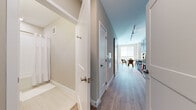 This single-floor residence offers a thoughtfully designed layout that balances comfort and functionality. A central hallway connects the key living areas, finished with smooth hardwood-style flooring that runs throughout the space and contributes to a cohesive, contemporary aesthetic.

The kitchen is fitted with rich dark wood cabinetry, granite countertops, and a full suite of stainless steel appliances including a refrigerator, range, and microwave. Track lighting overhead ensures the workspace is well-illuminated. Adjacent to the kitchen, the dining area provides a welcoming space for meals, bathed in natural light from nearby windows.

The living area is bright and inviting, featuring large windows with roller blinds that allow for flexible light control. A comfortable seating arrangement, anchored by a neutral-toned sofa and a wooden coffee table, creates an ideal space for relaxation. A circular wall mirror adds a decorative accent to the room.

The bedroom is a serene retreat, finished in soft neutral tones with warm ambient lighting and a set of built-in closets with white paneled doors, offering ample storage.

The bathroom is finished with clean white subway tile in the shower-tub combo, a dark wood vanity with a granite countertop, chrome fixtures, and light tile flooring — combining practicality with polished design.