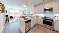 This well-appointed single-floor residence offers a cohesive and contemporary design throughout. The open-concept kitchen is a standout feature, showcasing white shaker cabinetry, granite countertops, a peninsula with pendant lighting, and a full suite of stainless steel appliances, including a dishwasher, range, microwave, and refrigerator. The kitchen flows seamlessly into the dining and living areas, which are finished with warm wood-look flooring and bathed in natural light from large windows with outdoor views. The living room provides a comfortable and functional layout, with space for seating and a wall-mounted television area. A dedicated dining nook sits between the kitchen and living space, offering an ideal setup for everyday meals or entertaining. The bedrooms are carpeted and serene, each benefiting from natural light and generous closet space. One bedroom features a walk-in closet with wire shelving that connects directly to a full bathroom, complete with tile flooring and a tub-shower combination. The overall aesthetic is clean and modern, with neutral tones, consistent finishes, and a bright, airy ambiance that carries throughout the entire residence.