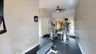 Located at 2379 Caringa Way in Carlsbad, California, this single-level fitness center offers a practical and well-appointed space for exercise. The room features durable rubber flooring throughout, providing a safe and supportive surface ideal for a variety of workouts. Neutral-toned walls and a ceiling fan contribute to a clean, comfortable environment during exercise sessions.

The space is outfitted with multiple elliptical trainers, a multi-station cable weight machine, and a weight bench, offering a well-rounded selection of cardio and strength training options. A wall-mounted flat-screen television adds convenience for entertainment during workouts. A large mirror spanning one wall visually expands the room while allowing users to monitor their form.

Natural light is a notable feature, with a glass-paneled door and adjacent windows providing views of lush greenery on one side, and a sliding glass door on the opposite end opening directly to a resort-style outdoor pool area. This seamless indoor-outdoor connection enhances the overall ambiance of the fitness center, making it feel bright and inviting. A wall-mounted hand sanitizer dispenser and additional interior door suggest thoughtful amenity-level planning throughout the space.