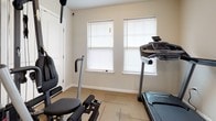 Located at 200 Cavalier in Petersburg, Virginia, this single-floor space is configured as a dedicated fitness room, offering a practical and functional environment for exercise. The room features neutral, light-toned walls that contribute to a clean and open atmosphere, complemented by carpet tile flooring laid in a grid pattern that provides durability underfoot.

Natural light enters through two standard windows fitted with white horizontal blinds, allowing for adjustable brightness throughout the day. A dedicated exterior entry door with a window panel and automatic door closer provides direct access to the space, adding convenience for users. A secondary interior door with glass panels connects to an adjacent area.

The room accommodates a variety of fitness equipment, including a ProForm treadmill, a Spirit recumbent exercise bike, a multi-station cable weight machine, and additional strength training equipment. A workout reference chart is posted on the wall for easy guidance during exercise sessions. The layout is organized to allow reasonable circulation around each piece of equipment. Overall, the space presents a straightforward, no-frills fitness environment suited for consistent, varied workout routines.
