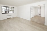 Located at 8 Grant Blvd in Hamilton, Ontario, this single-floor unit presents a clean, modern interior defined by a consistent neutral palette and light-toned wood-style flooring that flows throughout the space. The open layout, visible in the floor plan, connects the living, kitchen, and bedroom areas in a logical and functional arrangement.

The living area is bright and uncluttered, featuring large windows with black frames that allow natural light to fill the room while offering views of surrounding greenery. A radiator unit provides heating, and the light flooring enhances the sense of openness. An adjacent room features the same flooring and connects seamlessly to the rest of the unit.

The kitchen is well-appointed with white high-gloss cabinetry extending to the ceiling, white tile backsplash, light countertops, a stainless steel sink, and stainless steel appliances including a dishwasher and range. A window above the sink brings in natural light.

The bedroom includes a built-in closet and window with outdoor views. A dedicated entry area features built-in shelving with decorative detailing and lower cabinet storage. The bathroom is finished in white tile with a vanity, mirror, and chrome fixtures, maintaining the unit's clean, minimal aesthetic throughout.