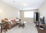 This single-floor residence offers a practical and comfortable layout designed for everyday living. The living area features plush carpeting, warm beige walls, and a large window with blinds that allows natural light to fill the space, creating a welcoming atmosphere. The kitchen is equipped with light wood cabinetry offering generous storage, tile flooring, a full suite of white appliances including a range, dishwasher, and refrigerator, as well as ample counter space for meal preparation. The bedrooms are carpeted and painted in consistent warm neutral tones, with each room offering windows that bring in natural light. One bedroom includes a built-in closet with a hanging rod, providing convenient storage. An additional room features a wall-mounted utility panel and serves as a versatile flexible space. The full bathroom is finished with tile flooring, a single-sink vanity with light wood cabinetry, a wall-mounted mirror with overhead lighting, and a tub-shower combination. Throughout the residence, clean white trim and neutral walls contribute to a cohesive, understated aesthetic. The dollhouse view reveals a well-organized floor plan that connects the living, kitchen, and bedroom areas efficiently, making the most of the available space.