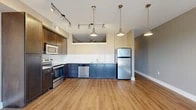 Located at 5350 Burnet Rd in Austin, TX, Unit 205 is a thoughtfully designed single-floor residence that makes efficient use of its space. The open-concept kitchen and living area serves as the heart of the unit, featuring warm hardwood-style flooring that flows throughout. The kitchen is well-appointed with rich dark-wood upper cabinetry contrasted by two-toned blue lower cabinets, white subway tile backsplash, light countertops, and a full suite of stainless steel appliances including a range, microwave, dishwasher, and refrigerator. Stylish pendant lights and adjustable track lighting illuminate the space, adding a modern, urban flair. The living area is open and airy, benefiting from natural light that pours in through a set of French doors, which also provide access to an outdoor view. A ceiling fan adds both comfort and character to the room. Neutral-toned walls throughout create a clean, versatile backdrop. The hallway connects the main living space to the bathroom, which features a tiled shower-tub combination and tile flooring. A dedicated closet provides practical storage. The overall ambiance is modern and functional, suited for contemporary urban living in Austin's vibrant Burnet Road corridor.