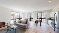 This contemporary single-floor residence showcases a thoughtfully designed open-concept layout that seamlessly connects the living, dining, and kitchen areas. Light hardwood flooring runs throughout the main living spaces, complementing the clean white walls and creating a bright, airy atmosphere. A defining architectural feature is the abundance of large, black-framed grid windows that line the living and dining areas, flooding the space with natural light while framing expansive urban views of the surrounding cityscape.

The living area offers generous proportions with room for comfortable seating and a dedicated dining space. The kitchen is efficiently designed with white cabinetry, dark countertops, and a full suite of stainless steel appliances, including a range, microwave, and dishwasher, with a window that continues the theme of natural light throughout.

The bedroom is a calm, neutral retreat finished with plush wall-to-wall carpeting and a large window with blinds for privacy. The bathroom features tile flooring, a white vanity with ample storage, a mirrored medicine cabinet, and a clean, white tub-shower combination. Overall, the space presents a modern urban aesthetic with a balanced blend of functionality and contemporary design.