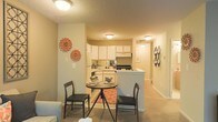 This two-floor residential space is designed with a practical and inviting layout that maximizes functionality. The main level features an open-concept living and dining area, where the dining space is positioned at the heart of the room, offering a natural gathering spot. The area is finished with warm neutral tones on the walls and soft carpeting underfoot, creating a cozy ambiance throughout.

The kitchen is seamlessly integrated into the open floor plan, separated from the dining area by a peninsula counter that provides additional workspace and a casual bar-style seating option. White cabinetry lines the kitchen walls, offering generous storage, while standard appliances including a range and refrigerator make the space fully equipped for everyday use. A textured ceiling adds a traditional architectural detail consistent throughout the main living areas.

A hallway extends from the main living space, leading to additional rooms and connecting the layout in a logical, easy-to-navigate flow. Flush-mounted ceiling lighting provides consistent illumination throughout, complementing the warm interior palette. The overall ambiance is comfortable and functional, with a straightforward design that prioritizes livability across both floors of the residence.