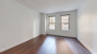 Located at 200 East Chestnut Street in Chicago's prestigious Streeterville neighborhood, this one-bedroom, one-bathroom unit offers a well-organized layout across a single floor. Rich, dark hardwood flooring flows consistently throughout the living areas and bedroom, providing a warm and cohesive aesthetic against the crisp white walls and clean white trim.

The living room is generously proportioned, featuring dual windows with roller shades that frame views of the surrounding urban architecture and welcome abundant natural light. The spacious bedroom continues the same hardwood flooring and neutral palette, with windows offering additional city views. It includes access to a dedicated closet, providing practical storage.

The galley-style kitchen is efficiently designed, featuring rich dark wood cabinetry, white countertops, and a full suite of stainless steel appliances including a gas range, built-in microwave, and refrigerator. The bathroom is finished with classic white subway tile surrounding a full bathtub, offering a clean and timeless look.

A hallway connects the rooms, contributing to a logical and comfortable flow throughout the unit. The consistent use of hardwood flooring, neutral tones, and natural light creates a bright, cohesive living environment ideally situated near Chicago's lakefront, dining, and shopping destinations.
