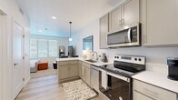 Located at 3040 Central Ave in Billings, Montana, this efficiently designed one-bedroom, one-bathroom unit offers a thoughtfully organized single-floor layout. The open-concept kitchen flows seamlessly into the living and sleeping areas, maximizing the use of the available space. The kitchen is outfitted with taupe shaker-style cabinetry, white quartz countertops, a stainless steel appliance suite including an electric range, built-in microwave, and dishwasher, as well as an L-shaped peninsula that doubles as a breakfast bar with seating. Pendant lighting adds a modern touch overhead. Light wood-look flooring runs through the kitchen and main corridor, while plush carpet covers the bedroom area. The spacious bedroom accommodates a full sleeping arrangement and benefits from a large window that invites natural light and views of the surrounding area, along with a walk-in closet. The bathroom features a clean, white palette with a single-sink vanity, white cabinetry, a large mirror, and wood-look tile flooring. Recessed lighting and bright white walls throughout contribute to an airy, modern ambiance that makes the space feel open and welcoming.