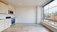 This single-floor unit showcases a clean, modern design with light-toned hardwood flooring carried consistently throughout the living spaces and bedrooms. The open kitchen and living area form the heart of the unit, where light wood cabinetry, white lower cabinets, and stainless steel appliances — including a range and built-in microwave — create a functional and contemporary cooking space. Recessed lighting and a large side window allow natural light to fill the area, contributing to a bright, airy ambiance.

The bedrooms are well-proportioned and notably well-equipped with storage, featuring multiple built-in closets with wire shelving. One bedroom benefits from a wall of oversized gridded windows that frame urban views of surrounding brick architecture, flooding the room with natural light.

The bathroom is finished to a high standard, featuring large-format stone-look floor tiles, white subway tile surrounding the soaking tub and shower combination, brushed gold hardware, and a wood-toned vanity with clean countertops. The overall palette throughout the unit — crisp whites, warm woods, and neutral tones — creates a cohesive, contemporary aesthetic that feels both inviting and functional.