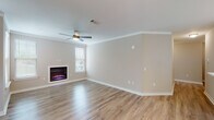 Located in Biloxi, Mississippi, this single-floor home offers a well-designed layout with modern finishes throughout. The living room serves as the heart of the home, featuring warm hardwood-style flooring, crown molding, a ceiling fan, and a sleek electric fireplace framed beneath a window that allows natural light to flow in. The open-concept layout connects the living area seamlessly to the kitchen, which is outfitted with crisp white shaker-style cabinetry, light countertops, stainless steel appliances including a refrigerator, range, and over-the-range microwave, and a peninsula with pendant lighting overhead. The primary bedroom is carpeted for comfort and includes direct access to a walk-in closet with built-in shelving and an en-suite bathroom featuring a white vanity, overhead cabinetry, and a shower. A second bedroom, also carpeted and equipped with a ceiling fan and natural light from a window, offers a comfortable and quiet retreat. The second full bathroom includes a tub-shower combination, a white vanity with a clean countertop, and wood-style flooring. A dedicated laundry room with hookups, overhead shelving, and exterior door access rounds out this practical and move-in-ready home.
