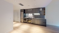Located at 1201 Half St SE in Washington, DC's Capitol Riverfront neighborhood, this single-floor residence showcases a clean, contemporary design throughout. Light wood-tone flooring flows seamlessly across the entire space, complementing the bright white walls and creating a cohesive, modern aesthetic.

The kitchen is a standout feature, outfitted with sleek charcoal flat-front cabinetry, stainless steel appliances including a gas cooktop and double wall ovens, and a full-size refrigerator. Recessed lighting illuminates the space, while generous counter space and open shelving add both function and style. A striking wood-grain entry door provides a warm contrast to the otherwise minimalist palette.

The living and bedroom areas are bathed in natural light, with a large picture window in one room framing a serene courtyard garden complete with greenery and a wood privacy wall — offering a peaceful, private outlook. Additional rooms feature clean lines, ample wall space, and closet access, providing versatile, well-proportioned layouts.

The bathroom is finished in a contemporary style with large-format white tile, a floating wood-toned vanity, an illuminated mirrored medicine cabinet, and a soaking tub with an overhead rain showerhead. Every detail reflects a refined, understated elegance suited for modern urban living.