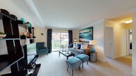 This single-floor residence offers a comfortable and thoughtfully designed layout across several well-defined living spaces. The living room serves as the heart of the home, showcasing crown molding, plush carpeting, and a large sliding glass door that floods the space with natural light and provides direct access to a private outdoor patio. The room comfortably accommodates a full seating arrangement and offers views of the surrounding greenery.

Adjacent to the living area, the dining room features crown molding, a large window with vertical blinds, and mirrored closet doors that enhance the sense of space. The galley-style kitchen is equipped with warm wood cabinetry, tile flooring, a full suite of white appliances, and ample counter space for meal preparation.

The two bedrooms are carpeted and tranquil, each offering natural light through windows with blinds. The primary bedroom includes a dresser area, while the second bedroom features dual closets for generous storage. Both bathrooms are finished with tile flooring and tub-shower combinations — one with a wood-toned vanity and tasteful décor, and the other clean and simply appointed. The overall ambiance throughout is warm and welcoming, with a neutral color palette that provides a versatile backdrop for any style.