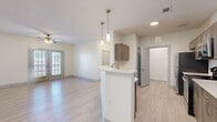 This thoughtfully designed 3-bedroom, 2-bathroom single-story home offers a bright, open layout with light wood-look flooring extending throughout. The combined kitchen and living area forms the heart of the home, where a peninsula kitchen with white quartz countertops, warm wood-toned cabinetry, stainless steel appliances — including a refrigerator and dishwasher — and elegant pendant lighting creates a functional yet stylish hub. The adjacent living room is generously proportioned, fitted with a ceiling fan, and opens to the outdoors through glass panel doors, inviting natural light and outdoor access. Three well-sized bedrooms each feature ceiling fans and light-filled windows with blinds, including one bedroom with dual corner windows. The primary bedroom is a comfortable retreat with access to a dedicated closet outfitted with built-in shelving. The bathrooms feature clean, modern finishes with wood-grain vanities and white quartz countertops. A dedicated laundry area houses a full-size washer and dryer with overhead shelving for added convenience. Three closets and a central hallway complete this well-organized, move-in-ready home designed for comfortable everyday living.