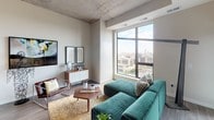 Located at 523 S 8th St in Minneapolis' Elliot Park neighborhood, this contemporary high-rise unit showcases an open, single-floor layout defined by striking exposed concrete ceilings, wide-plank hardwood flooring, and expansive floor-to-ceiling windows that frame sweeping panoramic views of the Minneapolis skyline and surrounding cityscape.

The open-concept kitchen is outfitted with white flat-panel cabinetry, quartz countertops, a subway tile backsplash, stainless steel appliances including a gas range, and pendant lighting — all beneath the dramatic concrete ceiling with track lighting. The living area flows naturally from the kitchen, anchored by large picture windows that flood the space with abundant natural light.

The bedroom is a well-appointed retreat featuring bold decorative wallpaper, tall windows with city views, exposed concrete ceiling details, a walk-in closet, and direct access to a hallway leading to the bathrooms. The en suite bathroom offers a dual-sink white vanity, quartz countertops, and a glass-enclosed walk-in shower with tiled surround. A second full bathroom includes a soaking tub and shower combo with a clean, neutral tile finish.

A dedicated workspace nook with a built-in desk and floor-to-ceiling windows completes this thoughtfully designed urban residence.