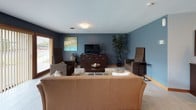 This single-floor space is thoughtfully designed with a cohesive, modern aesthetic highlighted by cool blue-grey walls, light wood trim accents, and durable tile-look flooring throughout. The open-concept living and dining area is generously sized, providing ample room for comfortable seating and a dedicated dining space. A large sliding glass door with vertical blinds floods the living area with natural light while offering direct views of a green outdoor space. Decorative artwork and tasteful furnishings contribute to the warm, inviting atmosphere of this room.

The kitchen is well-equipped and functional, featuring light maple cabinetry with brushed nickel hardware, granite-look countertops, and a full suite of stainless steel appliances including a refrigerator, electric range, over-the-range microwave, and dishwasher. The layout provides efficient workflow and ample cabinet storage. Recessed and flush-mount lighting ensures the space is well-lit throughout. Overall, the unit presents a clean, contemporary interior that balances practicality with a comfortable, livable ambiance.