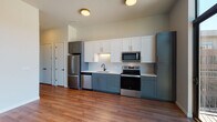 Located at 603 S Cascade Ave in Colorado Springs, Colorado, this single-floor unit offers a thoughtfully designed layout with modern finishes and striking views of the surrounding mountains. The open-concept living area is anchored by warm hardwood-style flooring that extends throughout the main spaces, creating a cohesive and inviting atmosphere.

The kitchen is a standout feature, showcasing a two-tone cabinet design with slate-blue lower cabinets and crisp white upper cabinetry, all accented with gold hardware. A textured geometric tile backsplash adds visual interest behind the stainless steel appliances, which include a refrigerator, electric range, microwave, and dishwasher. Light countertops complete the clean, contemporary aesthetic.

The living area benefits from an expansive floor-to-ceiling sliding glass door that opens to a private balcony, framing panoramic views of the Colorado mountains and filling the space with abundant natural light. A hallway connects the main living area to the bedroom, which features plush carpeting and generous built-in closet storage with wire shelving. The bathroom is finished with large-format marble-look tile in the tub surround, neutral floor tile, matte black fixtures, and a white vanity, delivering a clean and polished look.