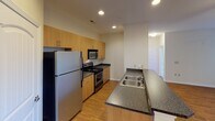 Located at 12930 S Tryon St in Charlotte, NC, this single-floor unit offers a practical and comfortable layout designed for everyday living. The open-concept living and dining area is finished with warm hardwood-style flooring and benefits from multiple windows fitted with blinds that allow natural light to fill the space. A ceiling fan overhead adds to the comfort of the room, which also features direct access to an exterior door. The kitchen is thoughtfully designed with light wood cabinetry, dark granite-style countertops, and a breakfast bar peninsula. Stainless steel appliances—including a refrigerator, gas range, and built-in microwave—are complemented by recessed lighting and durable hardwood-style flooring, creating a functional and attractive cooking space. The bedrooms are carpeted for comfort, with one room featuring notably tall ceilings that lend a sense of openness. A ceiling fan and window with natural light complete the secondary bedroom. The full bathroom is finished with a granite-top vanity with an undermount sink, white cabinetry, a large mirror, and a tiled shower-tub combination, all set on hardwood-style flooring. Clean neutral tones throughout the unit create a cohesive and move-in-ready environment.