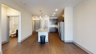 Located at 404 Gallop Ln. in Charlotte, NC, this single-floor residence offers a thoughtfully designed layout with contemporary finishes throughout. The kitchen is a standout feature, equipped with dark-toned shaker-style cabinetry, granite countertops, a subway tile backsplash, and a full suite of stainless steel appliances including a refrigerator, range, and built-in microwave. A kitchen island with a granite surface and undermount sink provides additional workspace and casual dining potential, while pendant lighting above adds an elegant touch. Rich, dark hardwood-style flooring extends through the main living and kitchen areas, complementing the neutral wall tones and creating a warm, cohesive aesthetic. The living area is spacious and bright, with a glass-paneled door that allows natural light to filter in. Bedrooms are finished with plush carpeting and feature windows with exterior views, and at least one room includes a ceiling fan for added comfort. The bathroom is clean and functional, featuring a tiled tub-shower combination with brushed nickel fixtures and granite vanity surfaces. A dedicated in-unit laundry room with a full-size washer and dryer adds everyday convenience. Wire shelving in the laundry area provides practical storage. The overall design balances modern style with functional living.