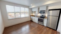 Located at 606 Burwell Street, Unit 313 in Bremerton, Washington, this single-floor residence features a contemporary design with a clean, modern aesthetic throughout. The open-concept layout is anchored by warm hardwood-style flooring that runs seamlessly through the living and kitchen areas, creating a cohesive and inviting atmosphere.

The kitchen is efficiently designed with a full suite of stainless steel appliances, including a refrigerator, electric range, built-in microwave, and dishwasher. Crisp white cabinetry — both upper and lower — provides ample storage, complemented by open shelving and neutral-toned countertops. Under-cabinet lighting adds a functional and polished touch. A window adjacent to the kitchen floods the space with natural light and offers views of the surrounding Bremerton streetscape.

The living area is generously proportioned, with clean white walls and recessed lighting that contribute to a bright, open feel. The bedroom is a well-sized, private room with its own entry door and continues the consistent flooring and neutral color palette found throughout the unit.

The bathroom is thoughtfully appointed with a wide vanity, under-sink cabinetry, a large mirror, and modern hardware. A frosted glass door provides privacy while maintaining a light, airy character. The overall design of this unit prioritizes functionality, clean lines, and a contemporary finish.