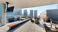 Located in Chicago's vibrant West Loop neighborhood at 123 N Desplaines, this expansive rooftop amenity level offers an impressive array of outdoor features across a generously sized single floor. The centerpiece of the space is a large covered pool surrounded by rows of lounge chairs, ideal for relaxation while taking in panoramic views of the Chicago skyline. Sleek glass railings line the perimeter, ensuring unobstructed sightlines of the surrounding cityscape, including notable high-rises and iconic towers.

The rooftop is divided into several well-appointed zones. A partially covered lounge area features a concrete overhead canopy, providing shade over clusters of stylish seating arrangements, including woven accent chairs, benches with warm wood accents, and dining tables suited for group gatherings. Multiple outdoor grills are positioned nearby, making this area well-equipped for entertaining.

A glass-enclosed interior section connects the outdoor spaces and is accented with lush vertical greenery, offering a bright, climate-controlled retreat. Additional open-air sun decks extend around the pool area, lined with chaise lounges bathed in natural light. A staircase and a bathroom round out the functional amenities. The overall design blends contemporary materials — glass, concrete, and tile — with a clean, modern aesthetic befitting its urban Chicago setting.