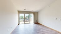 Located at 301 E Main St in Waunakee, Wisconsin, this one-bedroom, one-bathroom unit offers a well-organized single-floor layout designed for comfortable everyday living. The open-concept kitchen and living area serves as the heart of the home, featuring light wood-look flooring that runs throughout. The kitchen is equipped with rich dark-stained cabinetry, stainless steel appliances including a range, microwave, and refrigerator, a double sink, and a granite-topped island with pendant lighting overhead — providing both functionality and style. The living area is bright and airy, with neutral walls and a sliding glass door that opens to a private balcony, allowing natural light to fill the space and offering pleasant outdoor views. The bedroom is carpeted for comfort, features a dedicated closet with built-in shelving and hanging rods, and includes a window that brings in additional natural light. The bathroom is finished with tile flooring, a dark-stained vanity with ample drawer storage, a soaking tub, and a separate towel bar — creating a clean and practical space. Warm wood-tone trim and doors carry a consistent design language throughout the unit, giving it a cohesive and inviting feel.