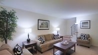 Located at 100 Fox Meadow Dr in Maple Shade, NJ, this two-story home offers a comfortable and well-appointed living environment. The main level features a spacious living room with soft, neutral-toned carpeting and warm white walls that create a bright and inviting atmosphere. The living room is anchored by a cozy seating area and accented with classic dark wood end tables and a matching coffee table, adding a touch of traditional elegance. A framed landscape artwork on the wall contributes to the room's refined yet approachable aesthetic. A staircase with a decorative wrought iron railing rises from the living area, serving as a focal point while providing access to the second floor. The overall design of the home embraces a timeless, neutral palette that allows for versatile decorating possibilities. The layout flows naturally between living spaces, making it well-suited for both everyday living and entertaining. The combination of carpeted floors, ample ambient lighting, and thoughtfully proportioned rooms gives the home a warm, lived-in character throughout both levels.