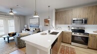 Located at 1875 Maple Dr in Kennesaw, GA, this well-appointed one-bedroom, one-bathroom residence offers a thoughtfully designed open-concept layout across a single floor. The kitchen serves as a central highlight, boasting a large quartz waterfall island with an undermount sink and pendant lighting, wood-tone cabinetry extending to the ceiling, and a full suite of stainless steel appliances including a french door refrigerator, range, and microwave. The island doubles as a breakfast bar with seating, seamlessly connecting the kitchen to the living area. The living room is bright and airy, featuring large windows with floor-to-ceiling drapes that invite natural light, light hardwood-style flooring, and neutral tones throughout. The bedroom offers plush carpeting, a ceiling fan, and generous window coverage providing natural light and a calm atmosphere. A dedicated closet provides practical storage. The bathroom features a glass-enclosed walk-in shower with white subway tile and brushed nickel fixtures, maintaining the clean, contemporary aesthetic found throughout the residence. Overall, the space exudes a modern, cohesive design with high-quality finishes.