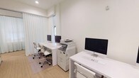 Located at 151 Du Rhu Dr in Mobile, Alabama, this single-floor office space embodies a clean, modern aesthetic defined by an all-white color palette and thoughtfully curated furnishings. The workspace is designed to accommodate multiple workstations, each outfitted with Apple iMac computers, sleek white desks, and ergonomic rolling chairs, creating a professional and cohesive environment throughout.

The space is bathed in natural light, which filters softly through floor-to-ceiling sheer white drapery, lending an airy, refined atmosphere to every corner. Recessed ceiling lighting complements the natural illumination, ensuring a consistently bright and productive environment. The flooring features a neutral woven texture that adds warmth while maintaining the minimalist tone.

A standout architectural feature is the use of glass partition walls with polished metal hardware, allowing visual connectivity between work areas while maintaining a sense of defined space. This open-yet-structured layout promotes both collaboration and focused individual work. A multifunction office printer is centrally accessible, adding practical utility to the design-forward space.

Decorative touches, including a framed landscape photograph and a lush indoor plant, introduce subtle organic elements that soften the crisp, white interiors. Overall, this office presents a sophisticated, light-filled workspace ideal for a professional setting.