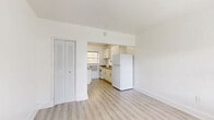 Located at 733 Palm Ave in Hialeah, FL, this single-floor unit offers a well-organized layout comprising a living room, kitchen, bathroom, and closet. The interior is finished with light-toned laminate wood flooring throughout, creating a clean and cohesive look across all rooms. Bright white walls reflect natural light, contributing to an open and airy atmosphere despite the compact footprint.

The living area is an open, unobstructed space bathed in natural light from a window overlooking the outdoors. A louvered bifold closet door provides convenient storage directly off the main living space. The entry door is a solid light-blue panel door, adding a subtle accent to the otherwise neutral palette.

The kitchen is accessible via an open pass-through from the living area and is equipped with white cabinetry—both upper and lower—featuring brushed gold hardware and granite countertops that add a touch of warmth. A white gas range, full-size refrigerator, and a window-unit air conditioner are included. The galley-style layout maximizes efficiency within the available space.

The bathroom is fully tiled in white, featuring a walk-in shower, a single vanity with an under-mount sink, and a small window that allows for natural ventilation. The consistent white-on-white design keeps the space feeling clean and bright throughout.