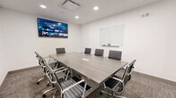 Located at 46120 Thomas Rd in Chilliwack, BC, this professional meeting room offers a clean, modern environment well-suited for business meetings, presentations, and collaborative sessions. The room is designed with a minimalist aesthetic, featuring crisp white walls and textured carpet flooring that lend a polished, corporate feel.

At the center of the space sits a large rectangular conference table with a wood-grain finish, surrounded by ergonomic high-back chairs with chrome frames — comfortably accommodating up to ten occupants. The room is equipped with a large wall-mounted flat-screen display on one wall, ideal for presentations and video conferencing, while a glass whiteboard mounted on the adjacent wall provides a sleek surface for brainstorming and note-taking.

Recessed ceiling lights provide bright, even illumination throughout the room, complemented by a ceiling-mounted ventilation unit that ensures a comfortable environment. A glass-panel door with a visible exit sign offers easy access and maintains an open, transparent connection to the surrounding office area. Built-in cable management features on the conference table support seamless connectivity for laptops and devices. Overall, the space delivers a functional and professional setting designed to facilitate productive meetings.