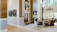 Located at 3134–3202 Sunset Blvd in West Columbia, SC, this expansive single-story clubhouse offers a generously proportioned gathering space designed with a modern aesthetic and high-end finishes throughout. The centerpiece of the space is a dramatic main lounge featuring soaring double-height ceilings clad in warm wood-paneled accent walls, a sleek linear fireplace, and curated artwork that adds visual interest at every turn. Large windows invite abundant natural light, creating an open and welcoming atmosphere. Adjacent seating areas are thoughtfully arranged, including a casual lounge with bold amber accent chairs grouped around a low coffee table, and a more refined sitting room with a neutral sofa set accented by yellow and navy throw pillows. Striking industrial-style sliding glass barn doors provide flexible division between zones. The kitchen and bar area is outfitted with dark stone countertops, a substantial central island, open shelving, a white penny-tile backsplash, built-in appliances, and a wall-mounted television — ideal for entertaining. A dedicated game room houses a full-size billiard table beneath recessed lighting. A private conference room with a long dark table, cane-back chairs, and a sculptural pendant light completes the offering, making this clubhouse equally suited for social gatherings and professional meetings.