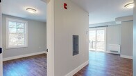 Located at 969 Hopmeadow St in Simsbury, Connecticut, this thoughtfully designed single-floor unit offers a clean, contemporary aesthetic throughout. The open-concept living and kitchen area is bright and welcoming, with natural light streaming in through multiple windows and sliding glass doors that lead to a private balcony overlooking the surrounding landscape. The kitchen is outfitted with crisp white shaker cabinetry, light quartz countertops, a classic subway tile backsplash, and a full suite of stainless steel appliances including a refrigerator, range, microwave, and dishwasher. Wood-look plank flooring flows consistently throughout the unit, lending warmth and visual continuity to every room. The additional bedroom is comfortably sized and features a large window that fills the space with natural light. The bathroom presents a refined finish with a dark-toned vanity, white countertop, and framed mirror. A utility area with white cabinetry and a utility sink adds practical functionality. The unit also includes an electrical panel and fire safety system, reflecting attention to both convenience and safety standards. Neutral wall tones and modern black hardware accents complete the polished, move-in-ready interior.
