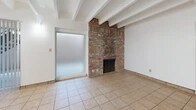 Located at 120 Cornell Dr SE in Albuquerque, New Mexico, this single-floor unit offers a well-organized layout comprising a combined living, dining, and kitchen area, one bathroom, two closets, and a private patio. Throughout the space, light-toned ceramic tile flooring provides a clean, cohesive look, while distinctive exposed wooden ceiling beams add architectural character and a sense of warmth to the interior.

The open living and dining area is a standout feature, highlighted by a full-height brick fireplace that serves as a natural focal point. A brass chandelier adds a classic touch overhead, and a pass-through counter connects the living area to the kitchen, enhancing the open feel. Sliding glass doors lead out to the private patio, filling the space with natural light.

The kitchen is efficiently designed with warm oak cabinetry, recessed lighting, a built-in range, and a full-size refrigerator, along with ample counter space for meal preparation. The bedroom area features two closets for generous storage. The bathroom includes a full tub-shower combination, a vanity, and tile flooring consistent with the rest of the unit. The exterior patio area provides additional outdoor space, accessible via a metal staircase with views of the surrounding Albuquerque neighborhood.