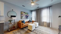 This thoughtfully designed single-floor residence blends modern aesthetics with practical functionality across a well-organized layout. The living area serves as the heart of the home, featuring soft blue-gray walls, warm wood-tone flooring, and a ceiling fan overhead. A rich cognac leather sofa anchors the space, complemented by a bold large-scale abstract artwork, a geometric patterned area rug, and floor-length striped drapes that frame windows allowing ample natural light.

The kitchen is a standout, showcasing two-tone cabinetry with crisp white uppers and charcoal gray lowers, a classic subway tile backsplash, and a full suite of stainless steel appliances. A central island with a white quartz countertop and seating provides an ideal space for casual dining, while pendant lights with glass shades add a refined touch overhead.

The bedrooms are bright and serene, each benefiting from large windows with blinds, ceiling fans, and wood flooring. Thoughtful storage is evident throughout, with utility areas including a dedicated laundry closet and additional storage spaces that enhance everyday convenience.

Throughout the residence, consistent light gray walls, clean trim work, and warm flooring create a cohesive, modern ambiance that is both inviting and versatile.
