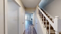 This two-story home is thoughtfully laid out across two levels, offering a functional and comfortable living environment. The main level is anchored by a spacious living room, where a white-painted brick fireplace serves as a striking focal point alongside wood-look laminate flooring that runs throughout. A large window adjacent to the front entry allows natural light to fill the space, contributing to a bright and airy atmosphere.

The kitchen features white cabinetry with brushed nickel hardware, crisp white countertops, a stainless steel sink, and a classic white subway tile backsplash that adds a clean, timeless aesthetic. A window above the sink brings in additional natural light.

A hallway on the main level connects multiple rooms and provides access to a bathroom equipped with a white vanity, white countertop, undermount sink, brushed nickel fixtures, a louvered medicine cabinet, and a beveled mirror. The textured walls and ceilings are consistent throughout the home.

Upstairs, a carpeted staircase with white balusters leads to the upper floor, where a bedroom features wood-look flooring, a ceiling fan, and direct access to a private bathroom. The overall palette is neutral and cohesive, creating a versatile and move-in ready environment.