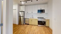 Located at 4240 Chestnut Street in Philadelphia's University City neighborhood, this efficient one-bedroom, one-bathroom unit offers a thoughtfully designed layout with modern finishes throughout. The open kitchen anchors the living space and is outfitted with stainless steel appliances — including a full-size refrigerator, dishwasher, and range — complemented by a built-in microwave, white upper cabinetry, warm-toned lower cabinets, a single-basin sink with a contemporary faucet, and a clean white countertop. Track lighting overhead provides excellent illumination. Warm hardwood-style flooring runs consistently throughout the unit, lending a cohesive and inviting feel. The bedroom is a well-proportioned, bright space with crisp white walls and is served by a dedicated closet featuring bifold doors and a full-width hanging rod for organized storage. The bathroom includes a walk-in shower stall with white subway tile surround and a chrome fixture. An overhead dollhouse view of the unit also reveals a window wall that brings in natural light and city views. The overall design is clean, contemporary, and functional — well-suited for those seeking a modern living space in a vibrant Philadelphia neighborhood.