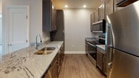 Located at 7 West St in Walpole, Massachusetts, this single-floor residence offers a well-designed layout with contemporary finishes throughout. The open-concept kitchen serves as a central hub, showcasing dark espresso cabinetry, granite countertops, stainless steel appliances including a refrigerator, range, and microwave, and durable hardwood-style flooring. A peninsula with a undermount sink adds both function and style, flowing seamlessly into the adjacent living area. The bedrooms are generously proportioned, each featuring plush carpeting, neutral-toned walls, and large windows that invite natural light and offer views of the surrounding building community. Two full bathrooms serve the residence — one featuring a walk-in shower with chrome fixtures and a granite-topped vanity with dark cabinetry, and the other providing a full soaking tub and shower combination with matching finishes. A dedicated in-unit laundry area accommodates a full-size side-by-side washer and dryer, adding notable convenience. The overall aesthetic is clean and modern, with consistent neutral tones, recessed lighting, and quality materials carried throughout the space, creating a cohesive and comfortable living environment.