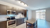 This modern single-floor residence offers a thoughtfully designed layout with clean lines and contemporary finishes throughout. The kitchen serves as a standout feature, equipped with a full suite of stainless steel appliances including a range, microwave, dishwasher, and refrigerator. Rich dark wood cabinetry lines the walls from floor to ceiling, complemented by speckled granite countertops and a white subway tile backsplash. A kitchen island with a matching granite surface provides additional prep and dining space. Track lighting overhead keeps the space bright and functional.

Light-toned hardwood flooring flows seamlessly throughout the main living areas and bedrooms, lending warmth and continuity to the interior. The bedrooms are bright and neutral, each benefiting from natural light through windows overlooking the surrounding building exterior. A spacious walk-in closet outfitted with wire shelving and hanging rods offers generous storage capacity.

Two full bathrooms maintain the home's modern aesthetic, featuring dark wood vanities with white countertops, large mirrors, and tile flooring. One bathroom includes a soaking tub and shower combination with white tile surround. A clean, well-lit hallway connects the private areas of the residence. The overall ambiance is bright, minimal, and move-in ready.
