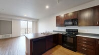 Located at 434 W Lake St in Minneapolis, Minnesota, this 1-bedroom, 1-bathroom unit offers a thoughtfully designed open-concept layout. The combined kitchen and living area forms the heart of the home, anchored by warm hardwood-style flooring that runs throughout. The kitchen is well-appointed with rich dark-wood cabinetry, granite-style countertops, a peninsula with an undermount sink, and a full suite of black appliances including a refrigerator, range, built-in microwave, and dishwasher. Track lighting overhead ensures the space is well-lit. The living area is bright and airy, benefiting from a large sliding glass door that opens to a private balcony, bringing in generous natural light and outdoor views of the surrounding Minneapolis neighborhood. The bedroom features a sliding-door closet and connects conveniently to the bathroom. The full bathroom is finished with large-format tile flooring, a dark-wood vanity with a white countertop, a wide mirror with bar lighting, and a tub/shower combination. Clean white walls and a neutral palette throughout give the unit a modern, cohesive feel. A dedicated closet provides additional storage within this efficiently designed home.