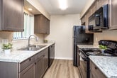 This two-story residence is thoughtfully designed across two levels, combining practical functionality with comfortable living spaces. The galley-style kitchen is well-appointed, featuring dark cabinetry with ample upper and lower storage, light granite-look countertops, a double stainless steel sink, and a full suite of black appliances including a refrigerator, electric range, built-in microwave, and dishwasher. Light wood-look flooring runs throughout the kitchen and main living areas, lending a clean, cohesive aesthetic.

The living areas are generously proportioned, each equipped with ceiling fans and textured ceilings. The main level includes a spacious living room with wood-look flooring and a large window allowing natural light to flow in. A staircase leads to the upper level, where bedrooms feature plush carpeting, ceiling fans, and natural light from windows with vertical blinds. Bedrooms include closet space, with at least one room offering a walk-in closet. The bathroom presents a clean, functional layout with a white vanity, toilet, and a tub-shower combination enclosed by a decorative curtain, accented by wood-look flooring.