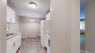 This well-laid-out one-bedroom, one-bathroom unit offers a comfortable and functional living space across a single floor. The kitchen is efficiently designed with white cabinetry, a full-size refrigerator, and a range, all complemented by wood-style plank flooring that extends into the adjacent dining area. A pendant light fixture hangs above the dining space, adding a touch of warmth. A textured ceiling and flush-mount lighting complete the kitchen area.

The spacious living room features neutral-toned carpet, a baseboard heating system, and a wall-mounted air conditioning unit, ensuring year-round comfort. A large window invites natural light and provides pleasant views of surrounding greenery, contributing to an airy atmosphere.

The bedroom is a comfortable, well-proportioned room with soft carpeting, a ceiling fan with light kit, and a window overlooking mature trees. Baseboard heating keeps the room warm, and the neutral wall tones create a calm, restful environment.

The full bathroom is clean and bright, featuring white square tile surrounding the tub-shower combination, wood-style flooring, a large mirror, and a vanity with a granite-style countertop, offering both style and practicality. Hallways connect the rooms efficiently, rounding out this practical and inviting space.